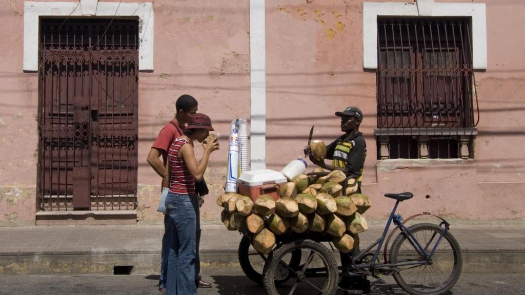 Coconut salesman on his bicycle in front of colonial building, Santo Domingo.